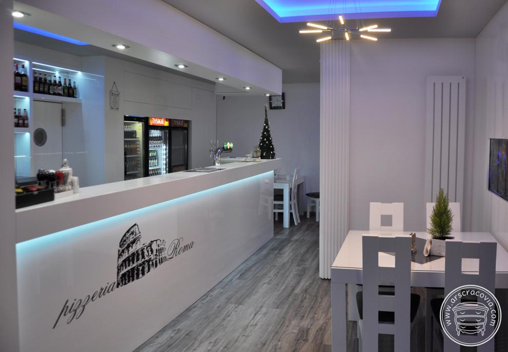 Wnętrze pizzerii z białym, podświetlanym barem z logo Koloseum i napisem 'Pizzeria Roma', jasnymi stolikami z krzesłami oraz nowoczesnym oświetleniem sufitowym z niebieską poświatą.