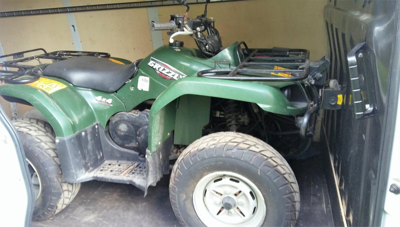 Zielony quad marki Grizzly 4x4 przewożony wewnątrz furgonetki z widocznymi elementami mocowania.