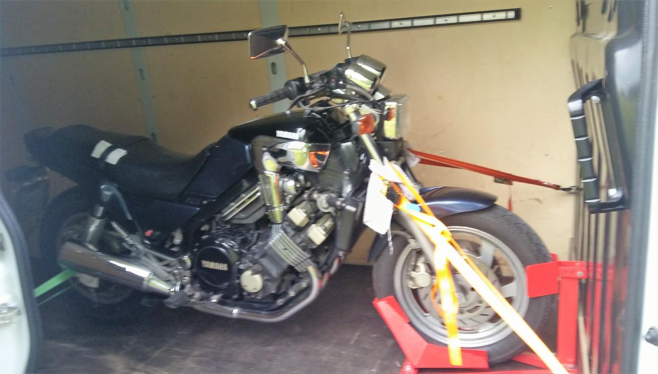 Czarny motocykl Yamaha zabezpieczony pasami transportowymi wewnątrz furgonetki, umieszczony na czerwonych stojakach pod koła.