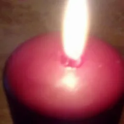 Płonąca, bordowa świeca kulista, blask płomienia oświetla wosk, widoczne drobne niedoskonałości powierzchni.