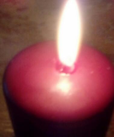 Płonąca, bordowa świeca kulista, blask płomienia oświetla wosk, widoczne drobne niedoskonałości powierzchni.