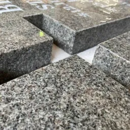 Fragmenty obrobionego, szarego granitu z widocznymi białymi napisami, prawdopodobnie elementy pomnika, czekające na montaż.