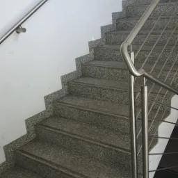 Granitowe schody wewnętrzne z metalową balustradą, widok z dołu, jasne ściany.