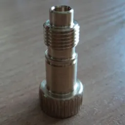 Mosiężny element z gwintem i radełkowanym pierścieniem, obrobiony na tokarce, leżący na drewnianej powierzchni.