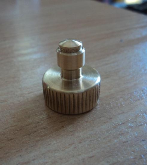 Mosiężny element metalowy z radełkowanym obwodem i stożkowym zakończeniem, leżący na drewnianej powierzchni.