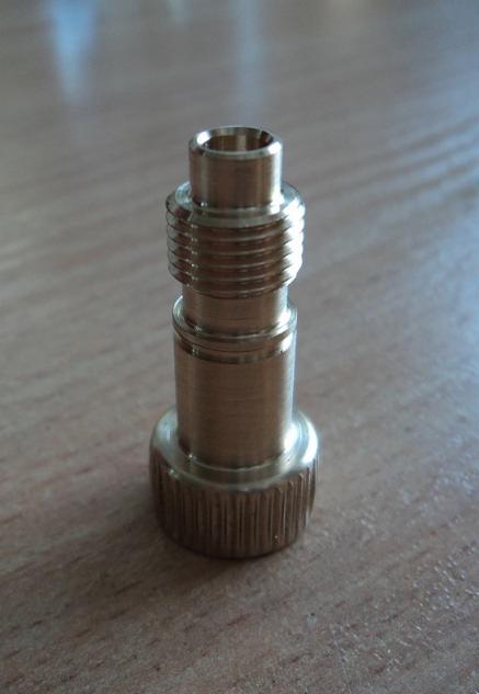 Mosiężny element z gwintem i radełkowanym pierścieniem, obrobiony na tokarce, leżący na drewnianej powierzchni.