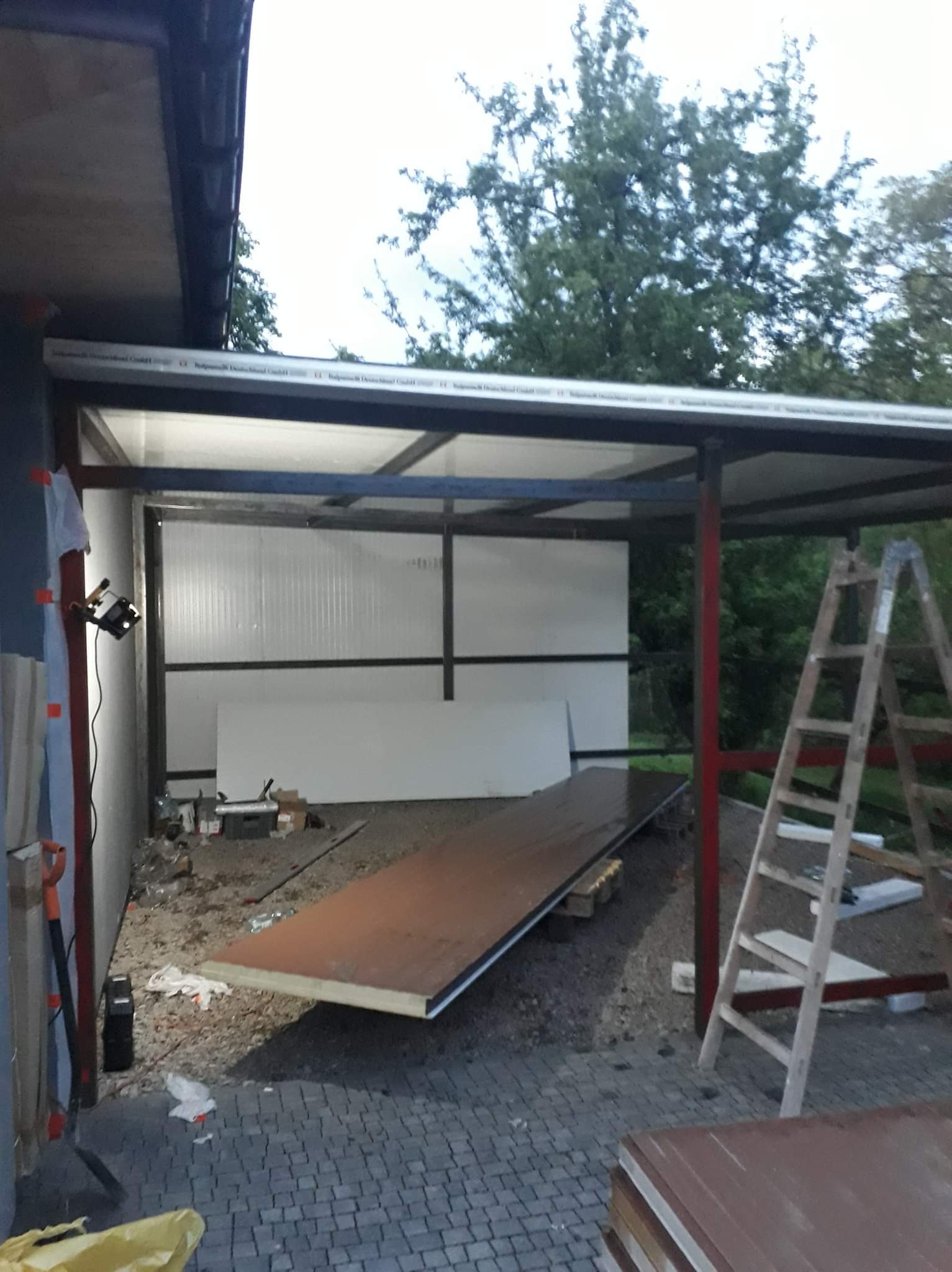 Montaż zadaszenia z płyt warstwowych w Świebodzicach, widoczne elementy konstrukcji stalowej, płyty przygotowane do montażu oraz drabina.