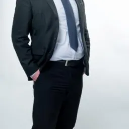 Portret mężczyzny w garniturze, stojącego na białym tle, z rękami w kieszeniach, prezentującego profesjonalny wizerunek.