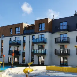 Nowoczesny budynek apartamentowy z balkonami i placem zabaw wodnych w słoneczny dzień.