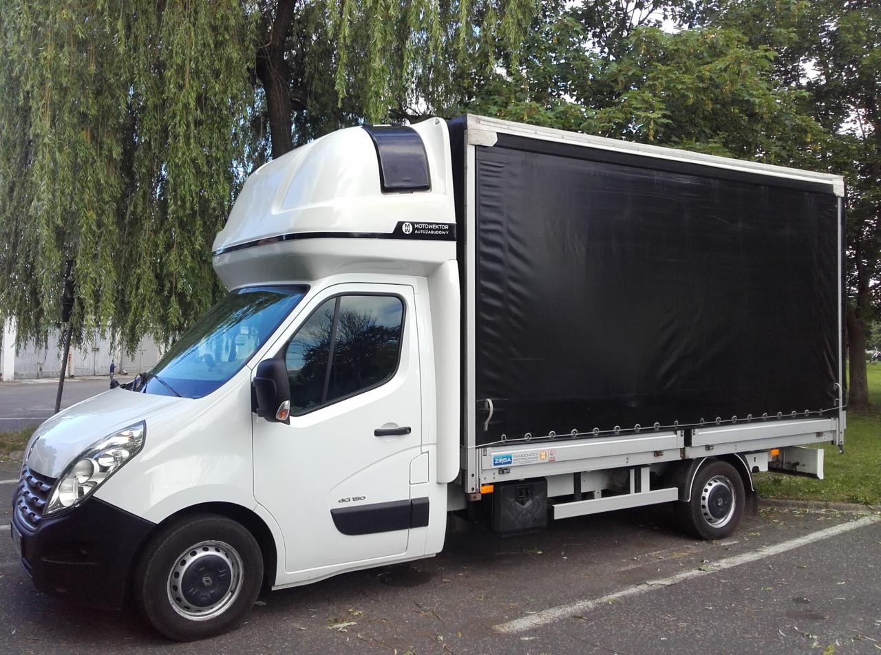 Biały samochód dostawczy Renault Master z czarną plandeką, zaparkowany pod drzewem, widoczny z boku, z nadbudową kabiny sypialnej.