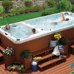 Przydomowy basen z hydromasażem i strefą do pływania, otoczony zielenią, z drewnianym tarasem i schodkami.