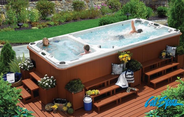 Przydomowy basen z hydromasażem i strefą do pływania, otoczony zielenią, z drewnianym tarasem i schodkami.