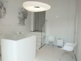 Jasne, minimalistyczne wnętrze recepcji z białymi meblami, okrągłą lampą sufitową i grafiką przedstawiającą popiersie kobiety na ścianie.