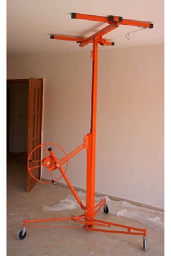 Pomarańczowy podnośnik do płyt gipsowo-kartonowych na kółkach, ustawiony w pustym pomieszczeniu z otwartymi drzwiami w tle, gotowy do montażu sufitu.