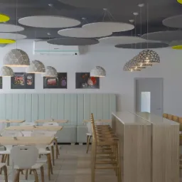 Nowoczesna jadalnia biurowa z jasnymi drewnianymi stołami, białymi krzesłami, wysokim blatem barowym z drewnianymi stołkami, miękkimi panelami ściennymi w kolorze miętowym, dekoracyjnymi lampami...