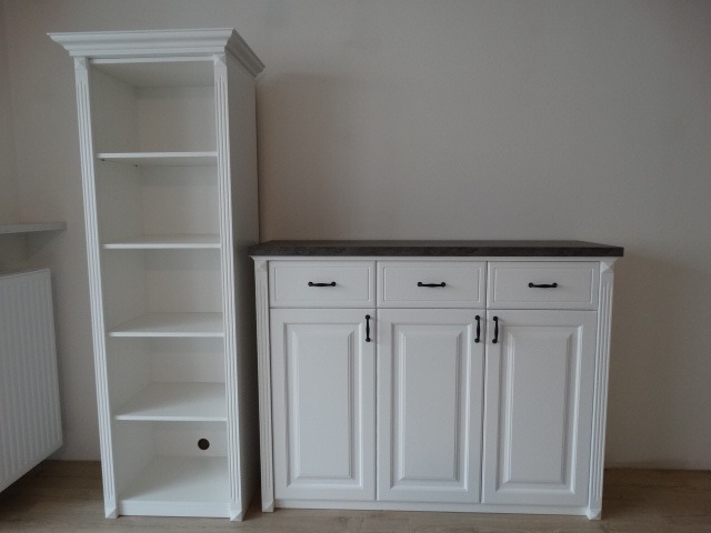 Biała szafka z szufladami i ciemnym blatem oraz wysoki regał z półkami, w stylu klasycznym.