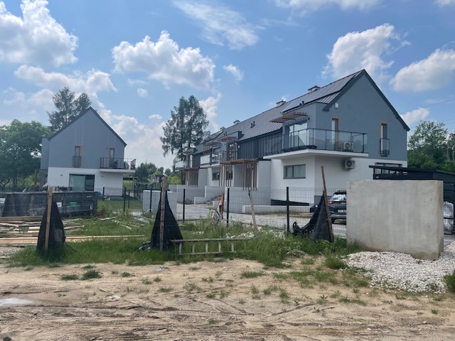 Kompleks szeregowy nowych domów z balkonami i szklanymi balustradami, widok z placu budowy z elementami konstrukcyjnymi i drabiną.