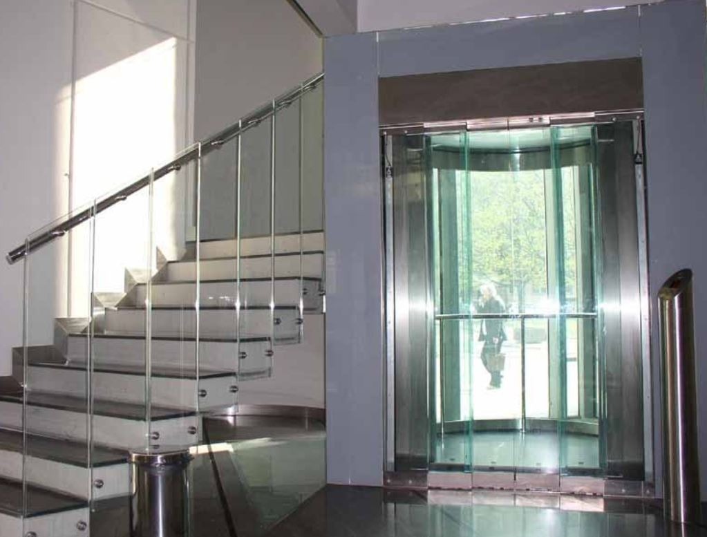 Szklana winda panoramiczna z widokiem na zewnątrz i schody ze szklaną balustradą w nowoczesnym holu.