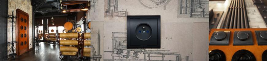 Czarny kontakt elektryczny na ścianie z wzorem technicznym, fragment industrialnego wnętrza z drewnianymi elementami i steampunkowym oświetleniem.