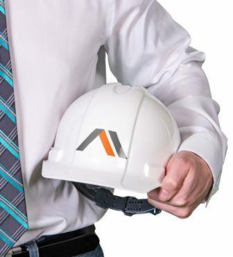 Biały kask z logo firmy w dłoni mężczyzny w koszuli i krawacie, symbolizujący usługi BHP i bezpieczeństwa pracy. Widok z bliska, neutralne tło.