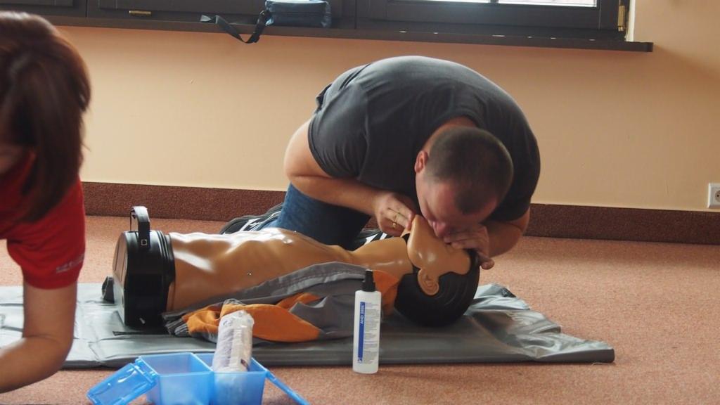 Szkolenie z pierwszej pomocy: mężczyzna wykonuje sztuczne oddychanie na manekinie, z widocznym zestawem ratunkowym i butelką z płynem dezynfekującym.