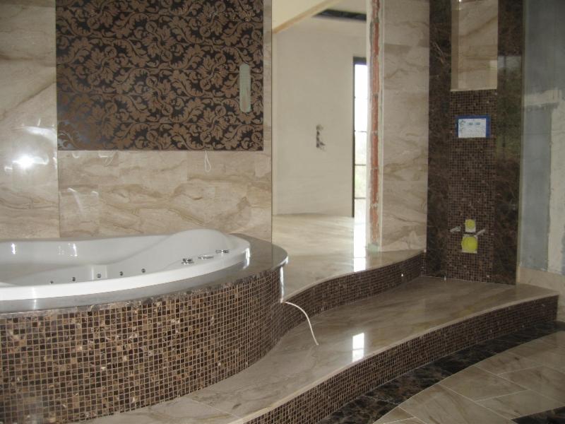 Łazienka w trakcie wykańczania z wanną z hydromasażem obudowaną mozaiką, marmurowe płytki na ścianach i podłodze, widoczne niedokończone elementy instalacji.