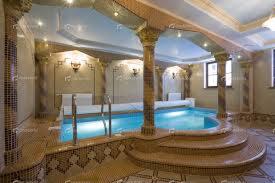 Luksusowy basen wewnętrzny z mozaiką, kolumnami i oświetleniem punktowym, otoczony niskim murem z poręczą ze stali nierdzewnej ułatwiającą wejście.