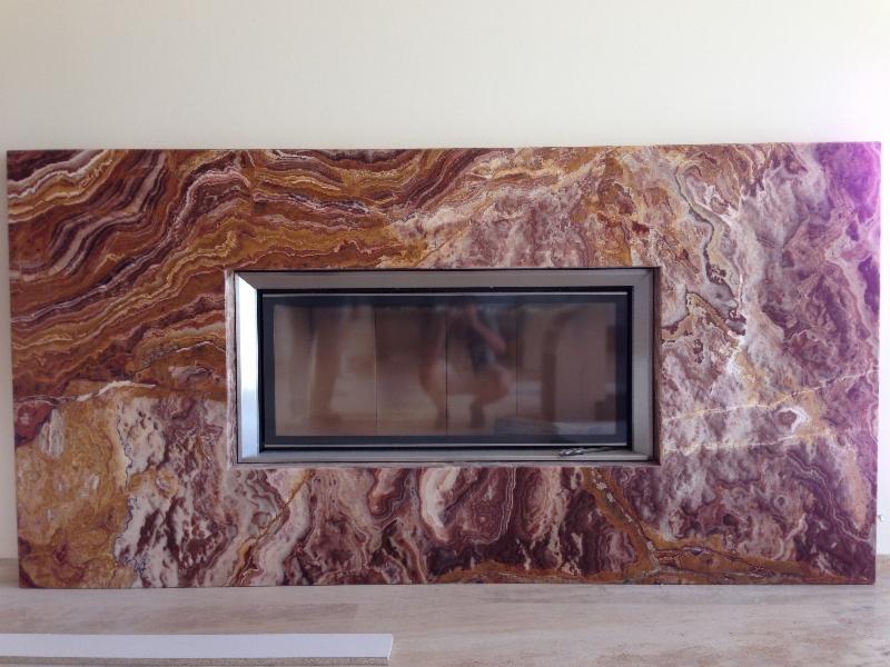 Obudowa kominka z polerowanego onyksu w odcieniach brązu i fioletu, z metalową ramą wkładu kominkowego.