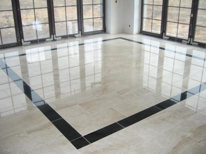 Beżowa marmurowa podłoga z czarną obwódką, odbijająca światło z okien w przestronnym, jasnym wnętrzu.