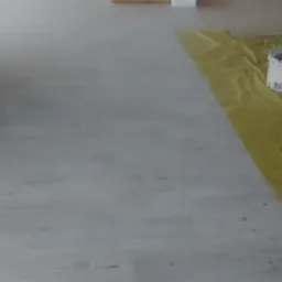 Jasne panele podłogowe ułożone w nowym pomieszczeniu, zabezpieczone folią malarską, z widocznymi materiałami izolacyjnymi i pojemnikiem z resztkami farby w tle.