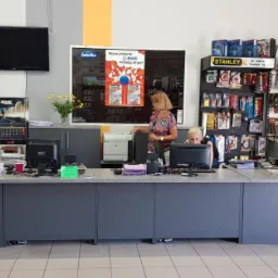 Wnętrze sklepu budowlanego: obsługa za ladą, regały z narzędziami Stanley i Solid, materiały budowlane, plakaty reklamowe Śnieżka i Mapei.