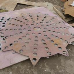 Anstal - Wycięte laserowo arkusze blachy z otworami o różnych średnicach i kształtach, ułożone na sobie. Widoczne ślady po cięciu i surowy wygląd materiału.