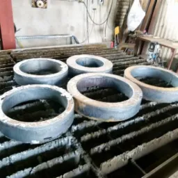 Metalowe pierścienie po cięciu plazmą, ułożone na stole roboczym z charakterystycznym wzorem. Widoczne ślady obróbki i minimalne nierówności krawędzi.