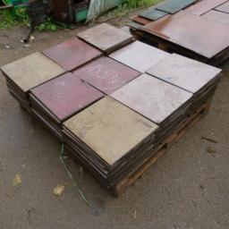 Anstal - Stos kwadratowych blach na palecie, niektóre z napisami, na zewnątrz, obok leżą inne blachy.