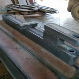 Stos metalowych elementów z otworem, po obróbce, o surowym wykończeniu, ułożonych na sobie. W tle widać inne metalowe detale i koło wózka widłowego.