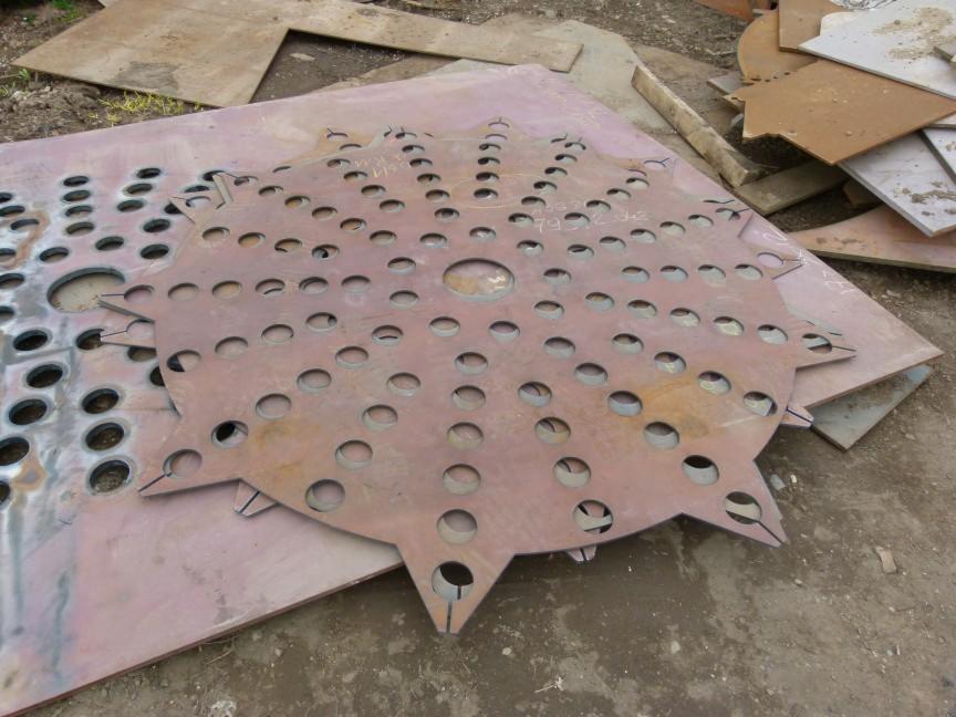 Wycięte laserowo arkusze blachy z otworami o różnych średnicach i kształtach, ułożone na sobie. Widoczne ślady po cięciu i surowy wygląd materiału.
