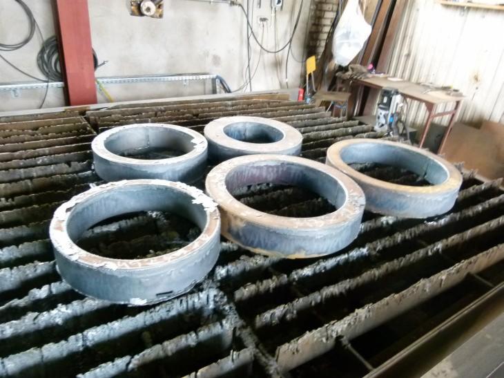 Metalowe pierścienie po cięciu plazmą, ułożone na stole roboczym z charakterystycznym wzorem. Widoczne ślady obróbki i minimalne nierówności krawędzi.