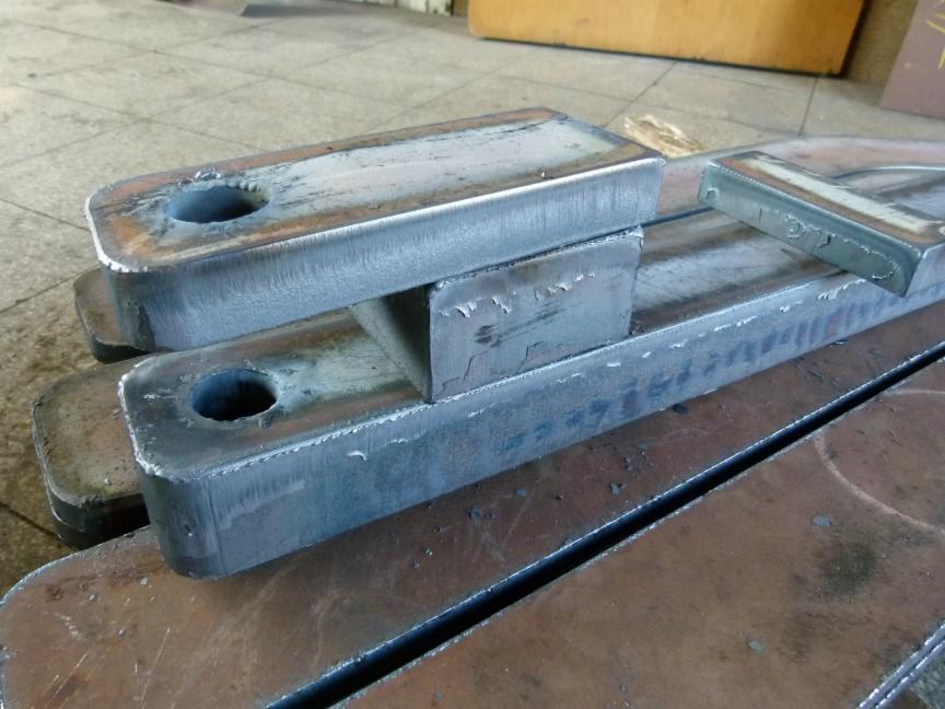 Surowe, metalowe elementy konstrukcyjne z otworem, ułożone warstwowo na metalowej powierzchni. Widoczne ślady obróbki i niedoskonałości materiału.