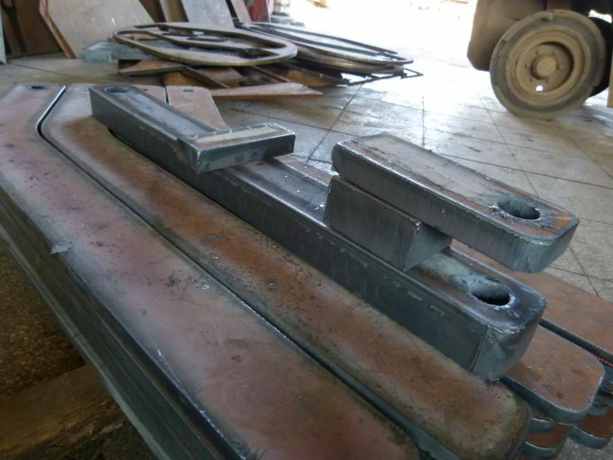 Stos metalowych elementów z otworem, po obróbce, o surowym wykończeniu, ułożonych na sobie. W tle widać inne metalowe detale i koło wózka widłowego.