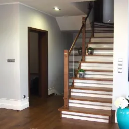 Nowoczesne schody drewniane z białymi akcentami, przeszkloną balustradą i roślinami w doniczkach. Parkiet w kolorze orzecha i turkusowy wazon z kwiatami.