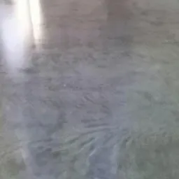 Szara, gładka powierzchnia podłogi z delikatnym wzorem, przypominającym przetarcia, odbijająca światło w górnym rogu.