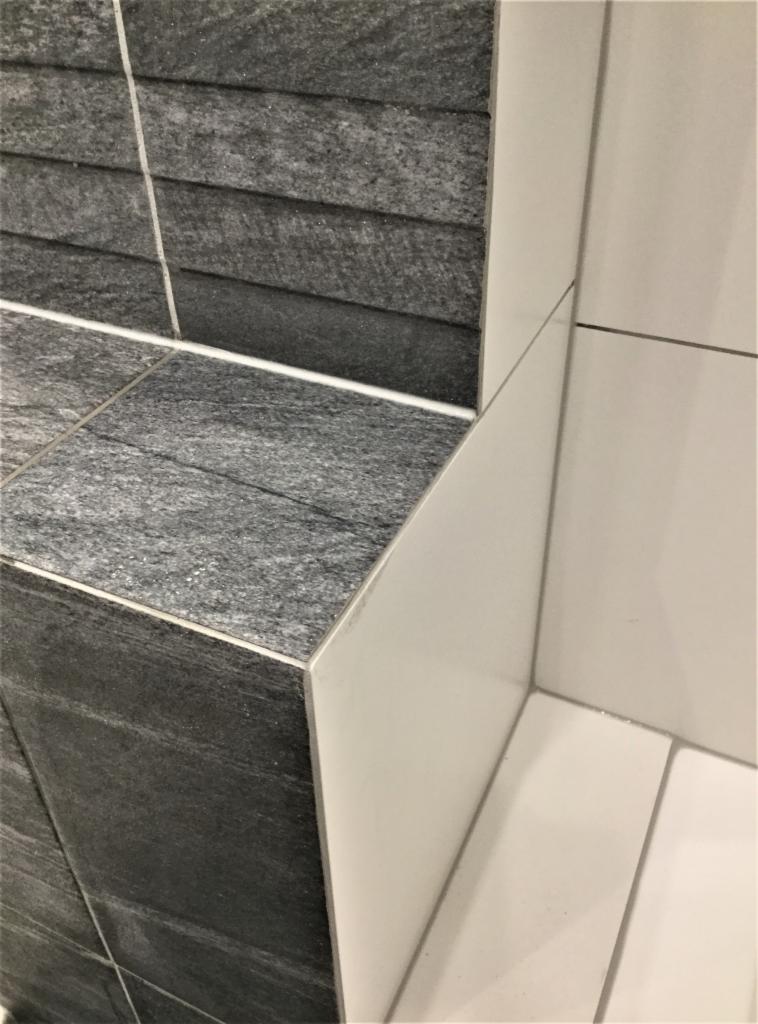 Szczegółowe ujęcie narożnika wykończonego płytkami w dwóch kolorach: grafitowym z teksturą i białym, z zaokrąglonym połączeniem płytek, ukazujące precyzję wykonania.
