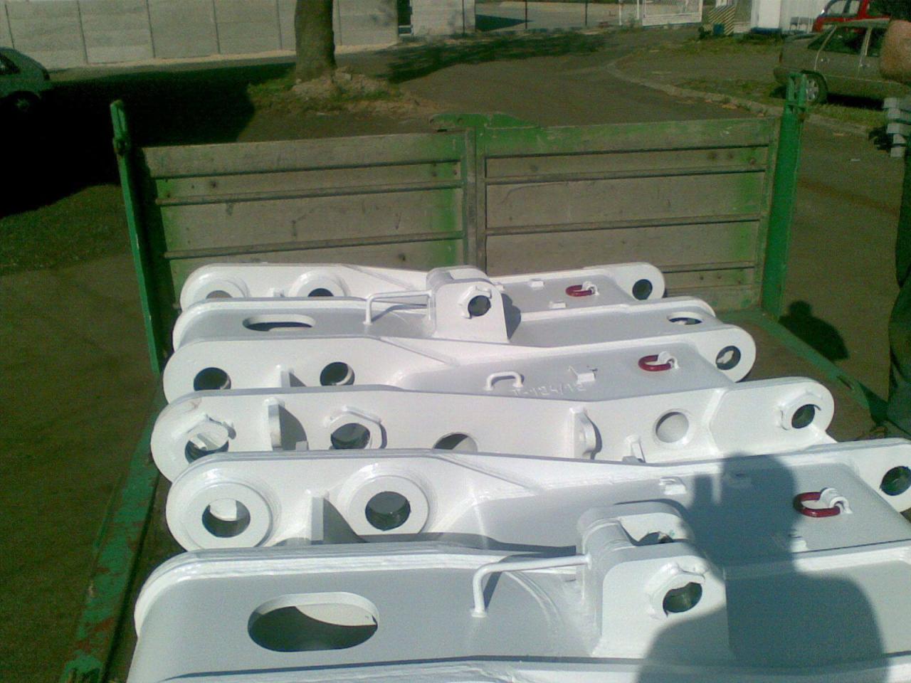 Białe, pomalowane elementy konstrukcyjne, prawdopodobnie stalowe, ułożone w skrzyni samochodu dostawczego. Widoczne otwory montażowe i ślady świeżej farby.