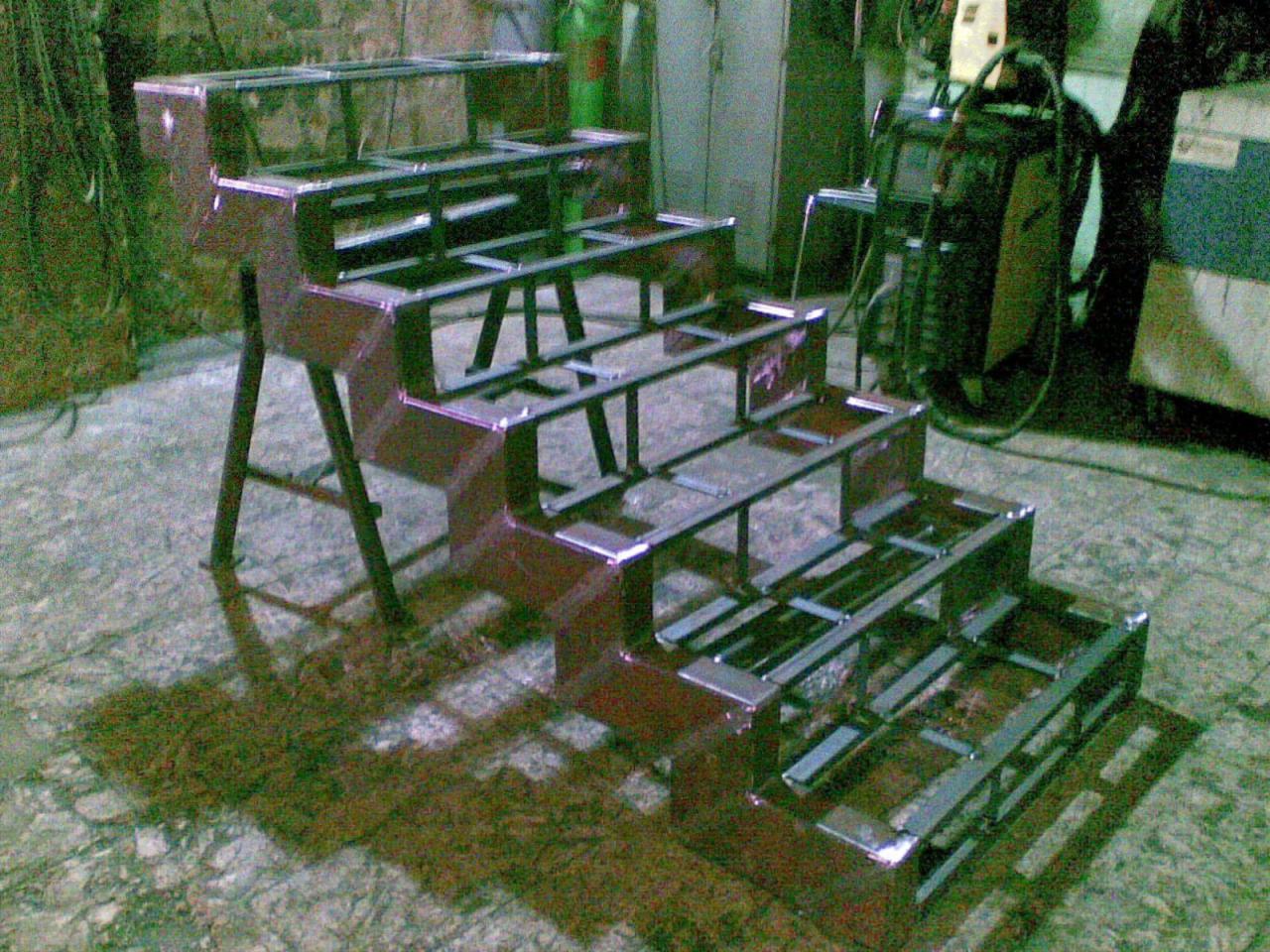 Niedokończona, metalowa konstrukcja schodkowa z profili stalowych, spawana, z widocznym spawarką w tle, na posadzce z terazzo.