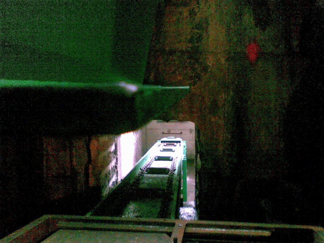 Wnętrze hali z suwnicą łańcuchową, widok wzdłuż toru jezdnego, oświetlenie punktowe w tle.