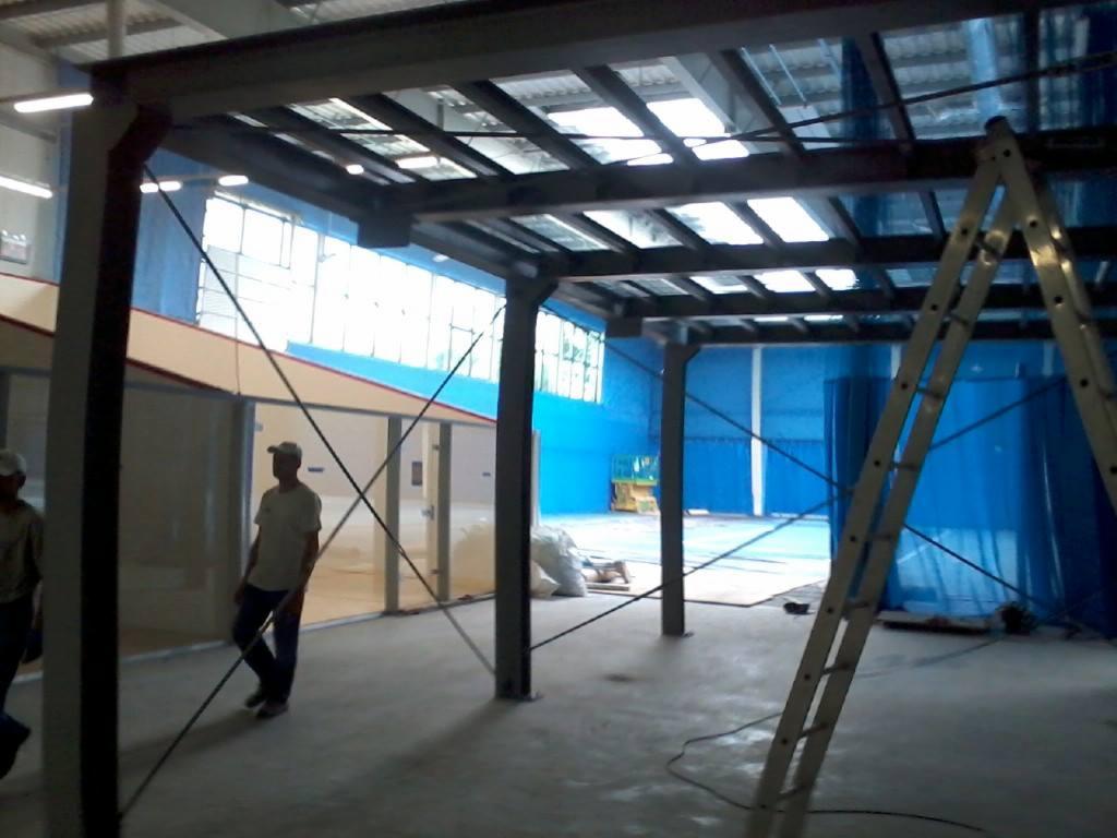 Montaż konstrukcji stalowej z widoczną drabiną w hali sportowej w Pszczynie, z elementami niebieskiej osłony. Widoczni pracownicy.
