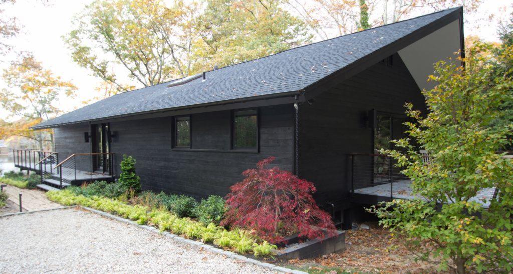 Nowoczesny, parterowy dom w Borne Sulinowo z czarną drewnianą elewacją i grafitowym dachem, otoczony zielenią i czerwonym klonem palmowym.