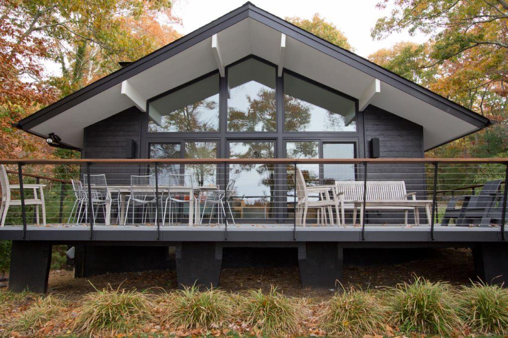 Czarny, nowoczesny dom z dużymi oknami i tarasem z metalową balustradą, otoczony drzewami z jesiennymi liśćmi.
