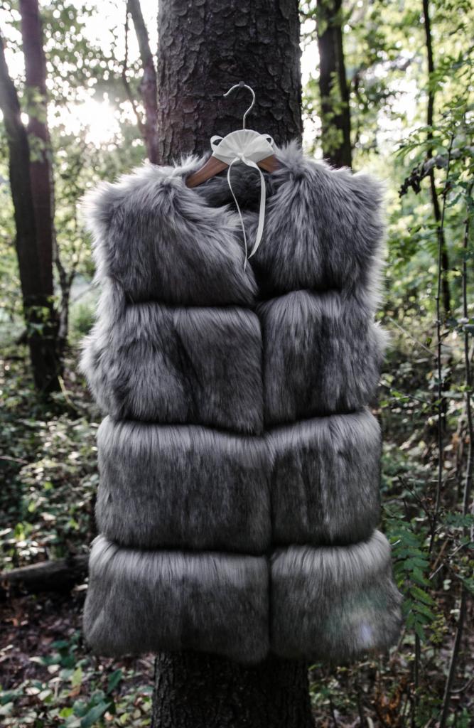 Szare futro na wieszaku zawieszone na drzewie w lesie, z delikatnym światłem słonecznym w tle, ukazujące unikalną fakturę i odcień futra.