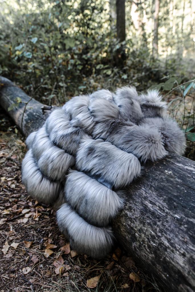 Szary, futrzany szal na spróchniałym pniu w lesie. Ułożony w dekoracyjny sposób, z widoczną strukturą futra i naturalnym tłem leśnym.